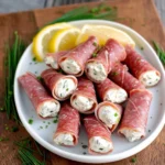 Creamy salami roll-ups with cream cheese and herbs served on a platter
