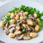 Creamy mushroom gnocchi served in a bowl with fresh herbs