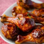 Oven-baked BBQ chicken drumsticks garnished with herbs, served on a plate.