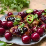 Plate of sticky cherry chicken thighs garnished with fresh cherries and herbs
