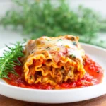 Plate of cheesy lasagna roll ups topped with marinara sauce and herbs.