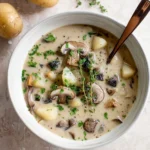 Creamy mushroom and potato soup in a bowl, garnished with herbs.