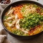Bowl of aromatic ginger scallion chicken noodle soup with fresh scallions and ginger.