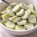 A bowl of creamy cucumber salad topped with fresh herbs and spices.