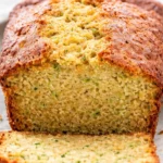 Loaf of homemade zucchini bread with fresh zucchini slices on the side.